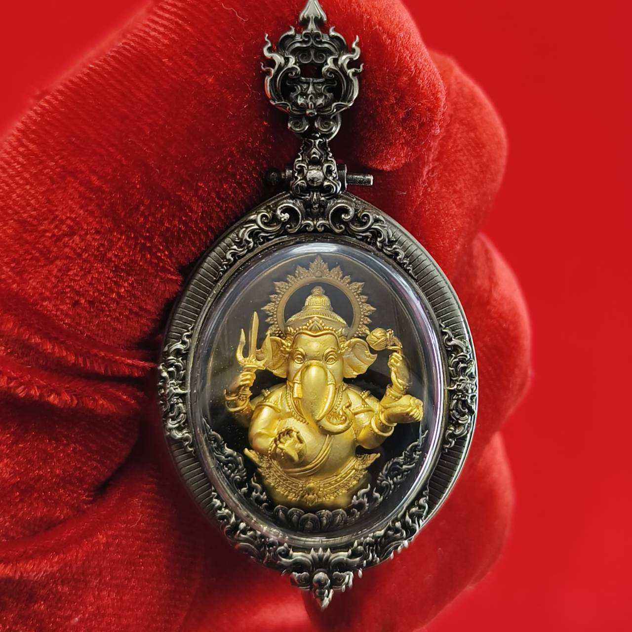 Thai Ganesh pendant white satin gold ornate oval amulet with gold Ganesh in decorative silver frame held against red background