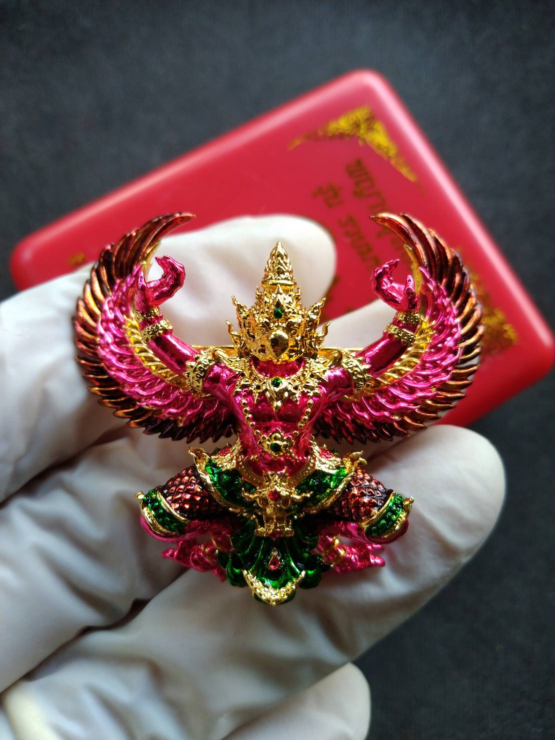 Garuda Phaya Krut Yok Tana Amulet Garuda Wealthy Millionaire Edition colorful gold pink green pendant held in gloved hand