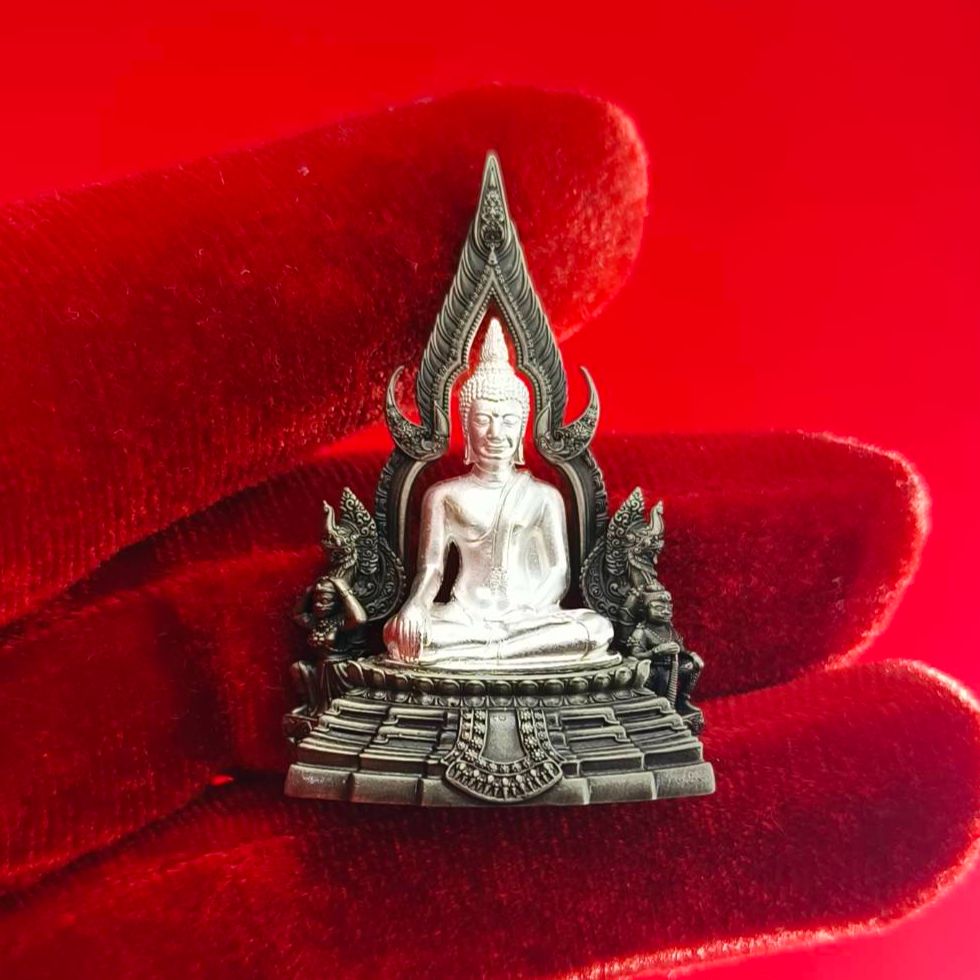Silver Phra Phuttha Chinnarat amulet on red velvet display held in hand with ornate base and flame halo