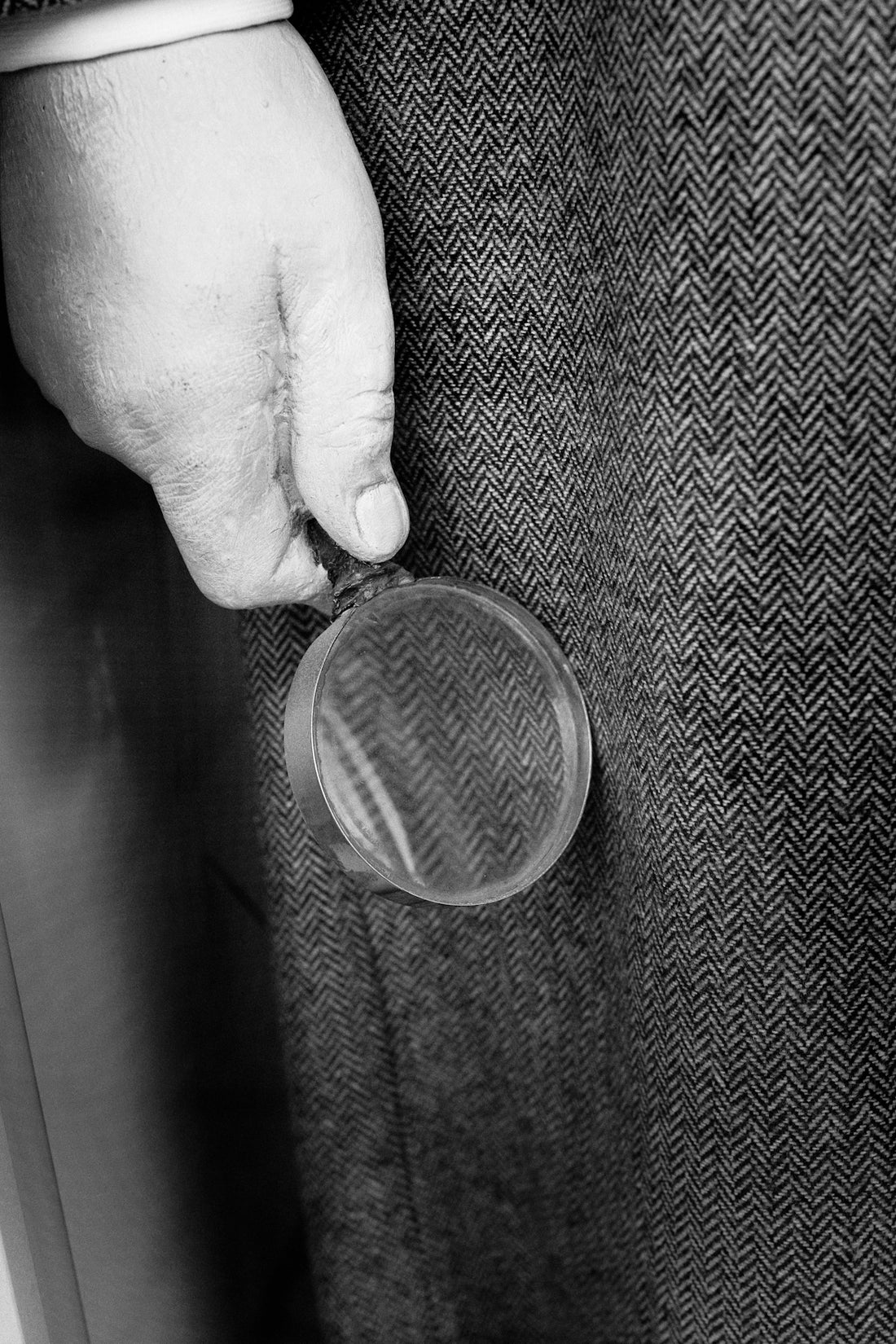A hand holds a monocle against textured fabric.