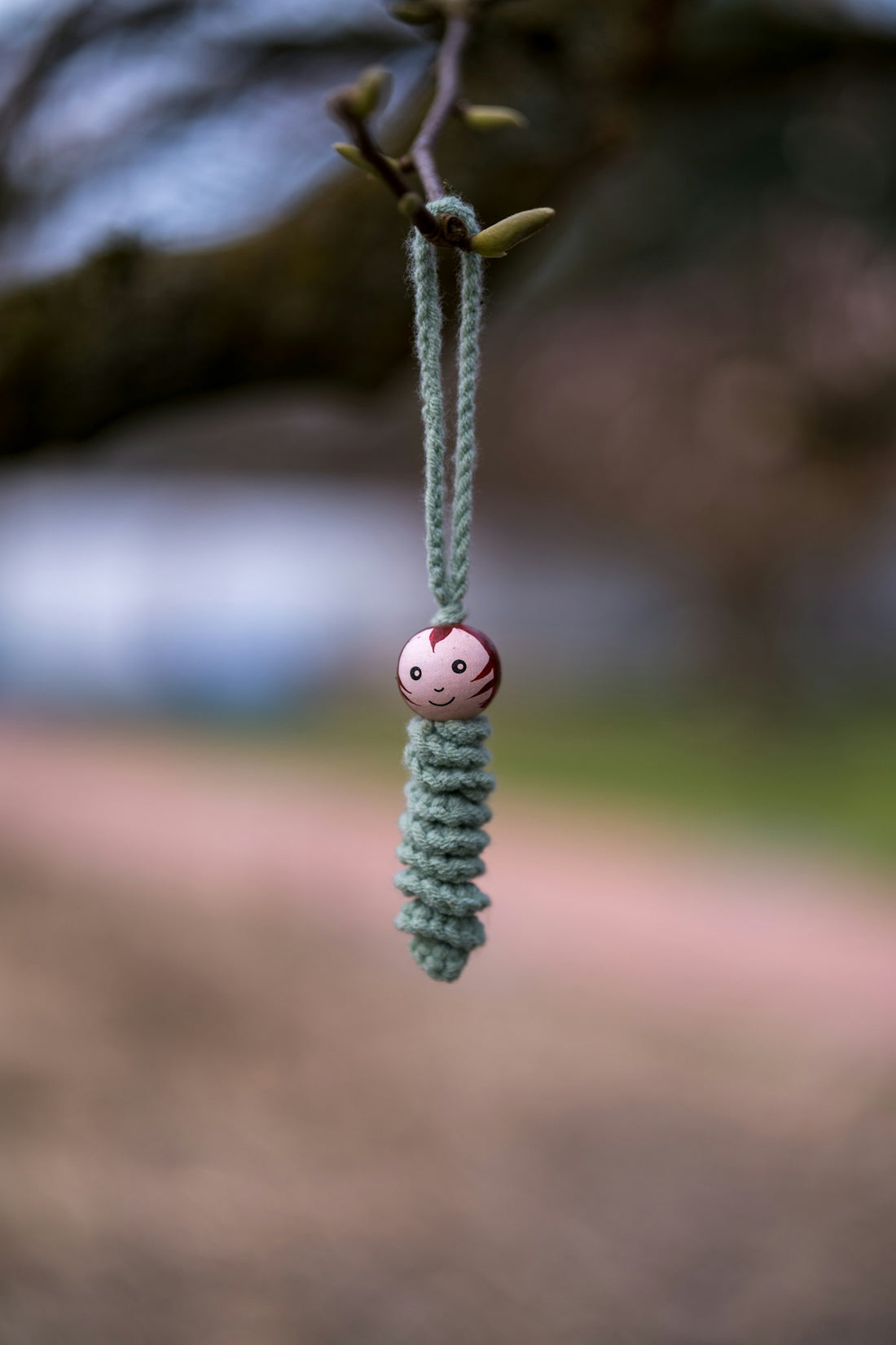 A small crocheted charm with a face hangs outdoors.