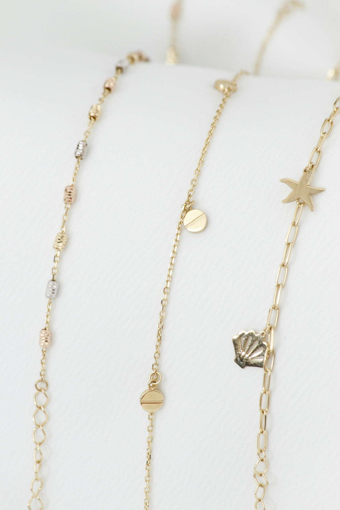 Three delicate gold necklaces with charms on white background