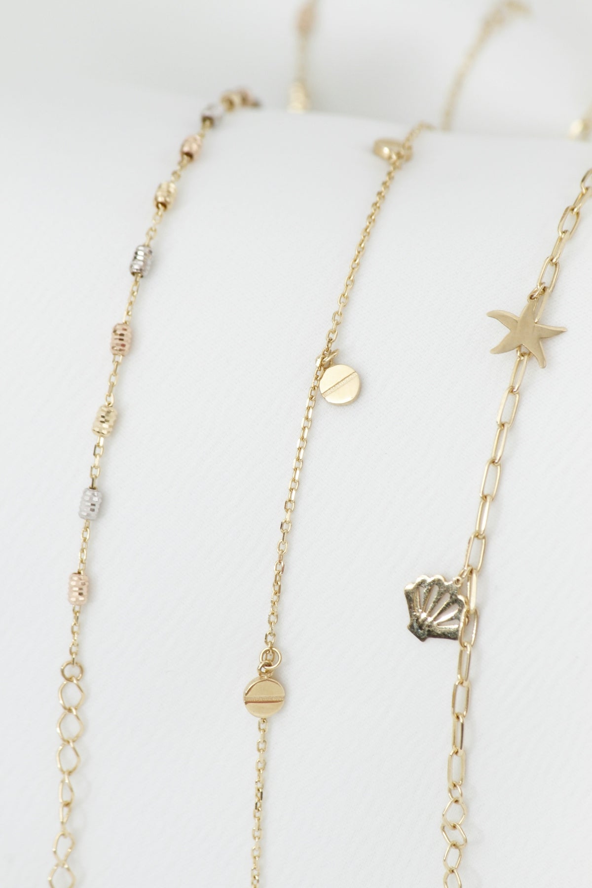 Three delicate gold necklaces with charms on white background