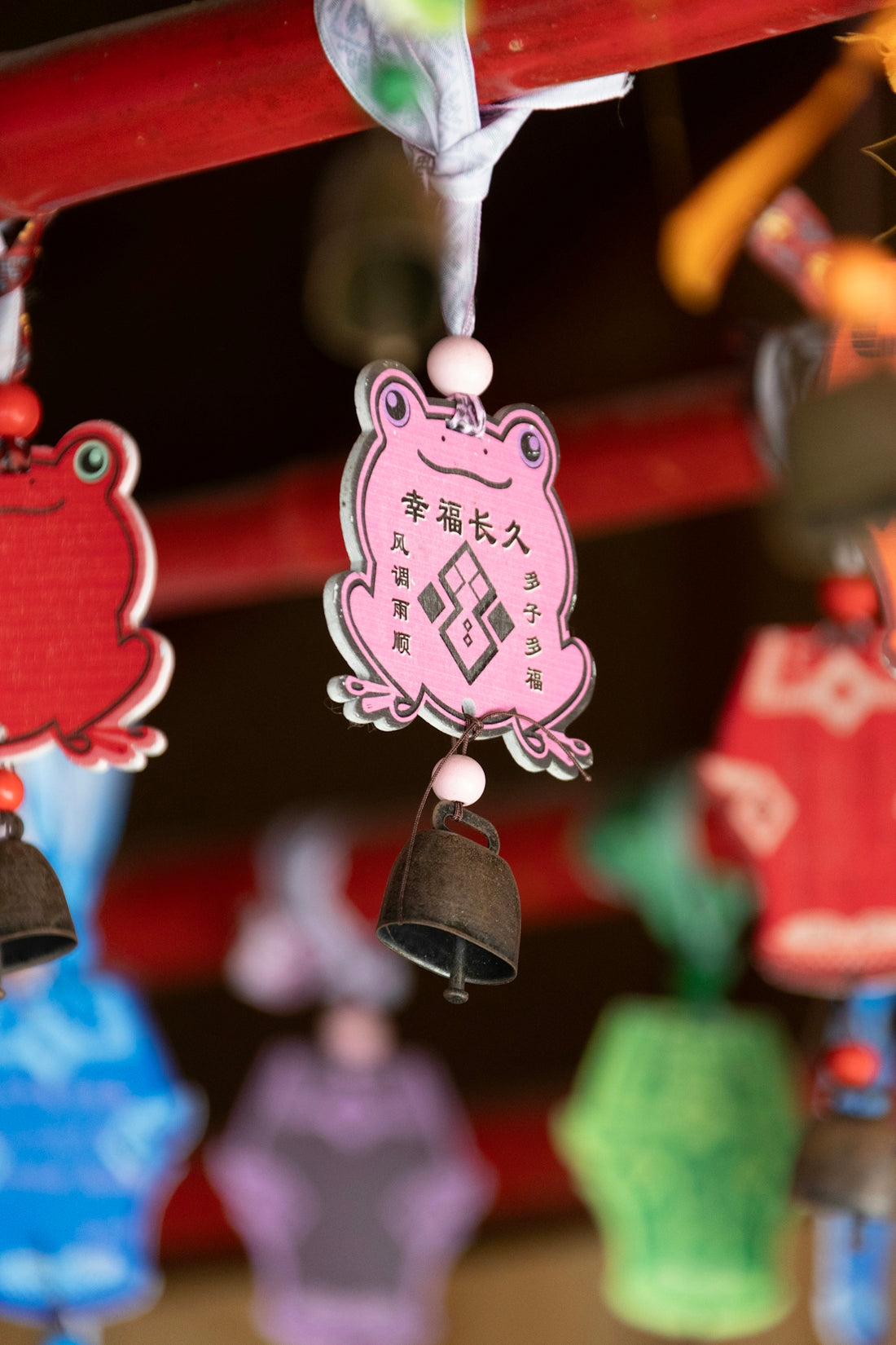 Pink frog charm with bell and chinese characters.