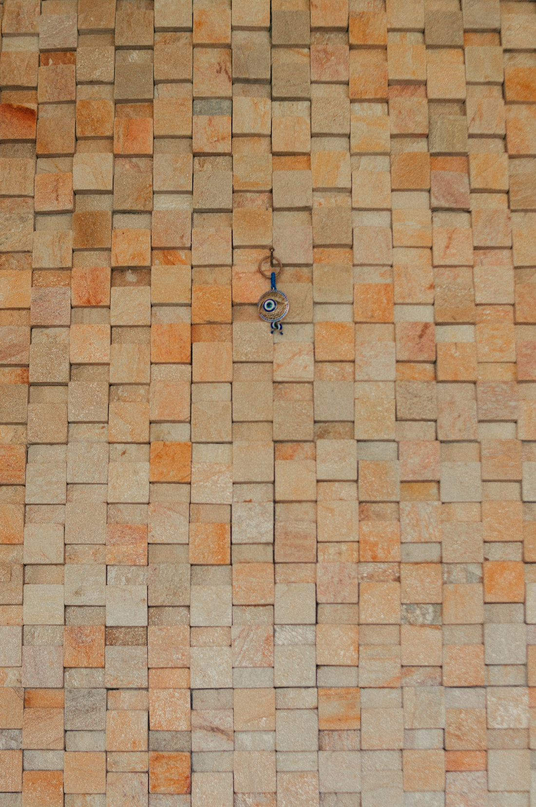 Evil eye charm hanging on a textured stone tile wall.