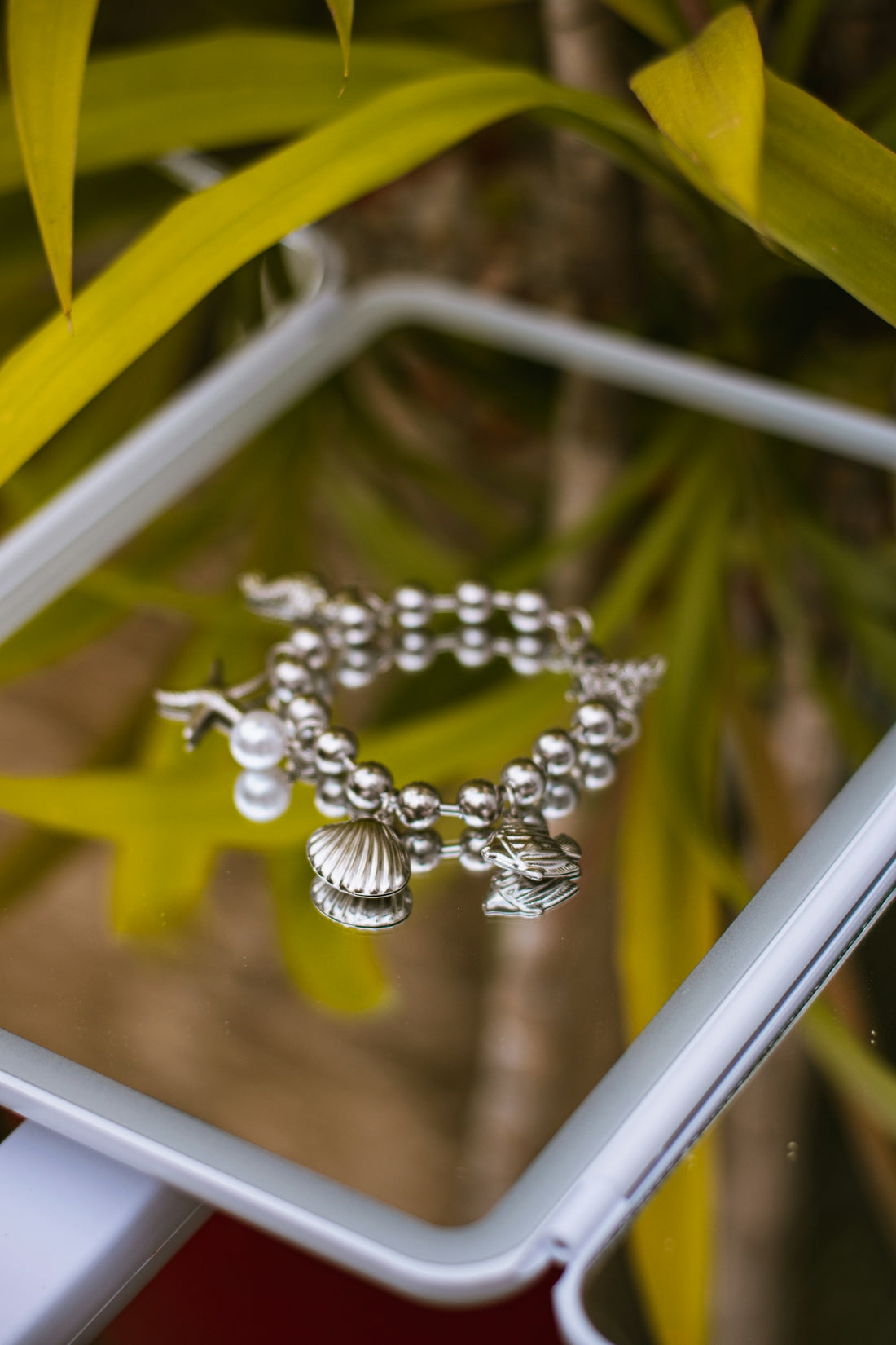 Silver charm bracelet with pearl, seashell, and fish on mirror.
