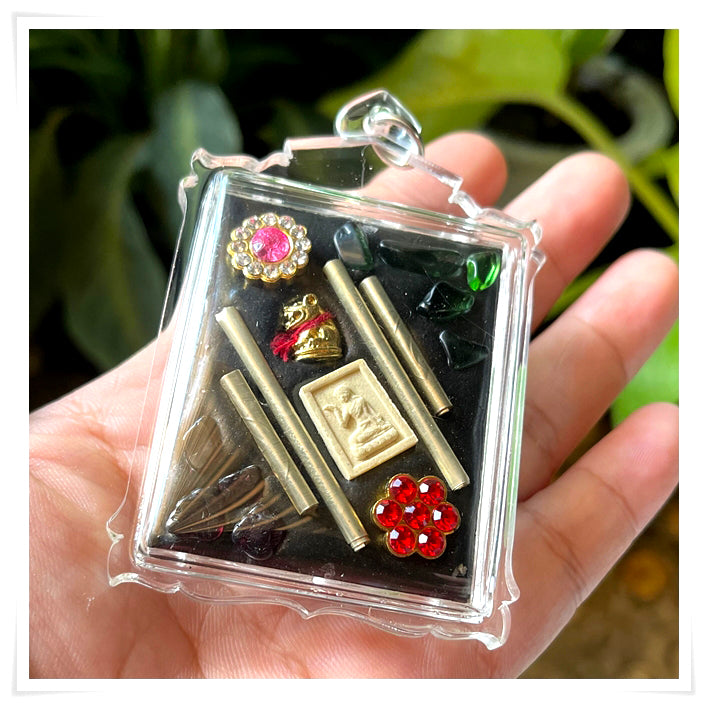 Phayak Naree tiger goddess amulet in clear plastic case with gold talismans, red jewels, and black backing held in hand