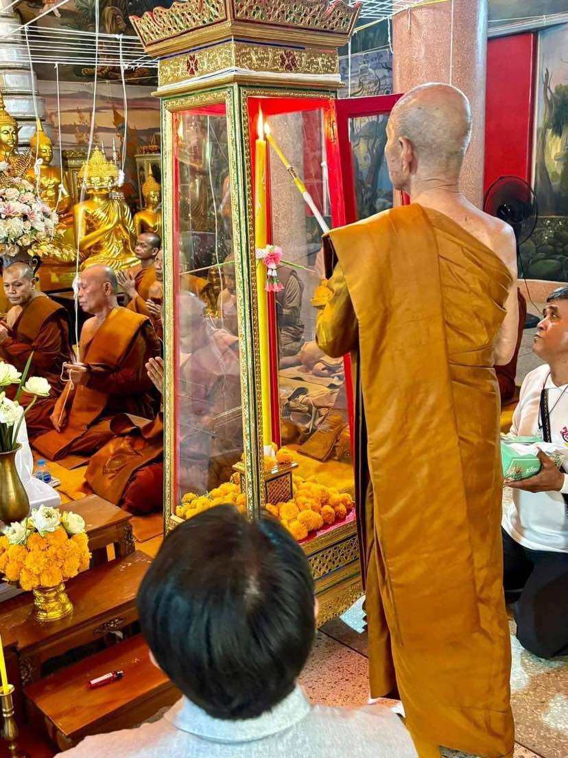 Monk blessing authentic Thai guardian amulet in ornate shrine with worshippers present