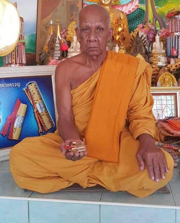 Monk in orange robe holding a Thai fortune charm bracelet in traditional temple setting