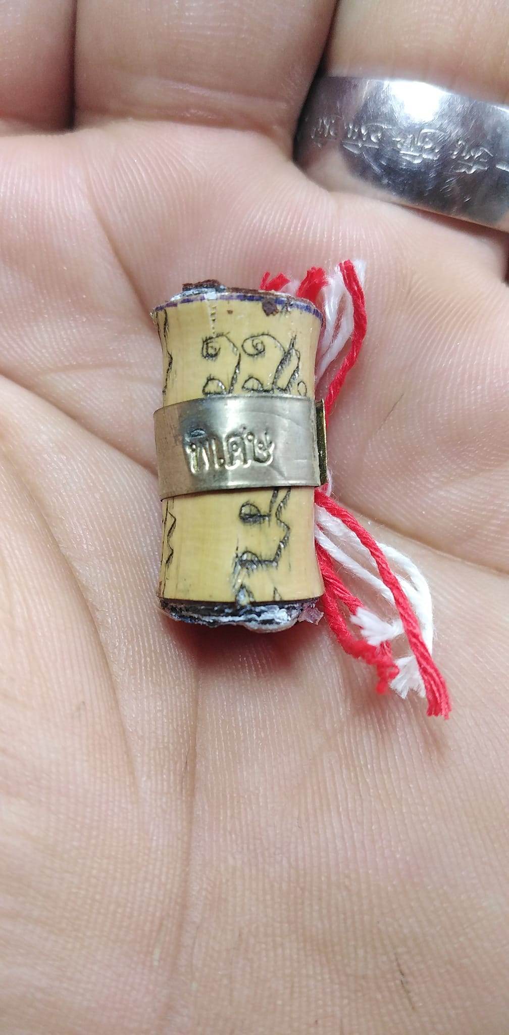Thai fortune charm bracelet scroll pendant with silver band and red white thread in hand