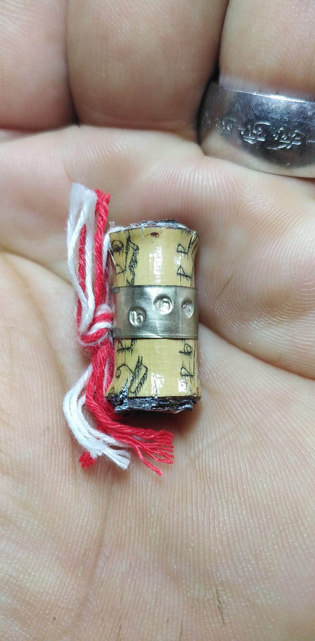 Close-up of Thai fortune charm bracelet scroll with red and white threads held in hand