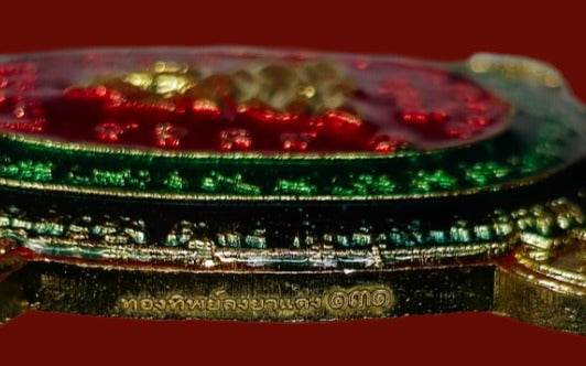 Close up side view of enameled gold amulet medallion with Thai script Phaya Tao Ruen Amulet Blessed by Phra Ajarn Uthai