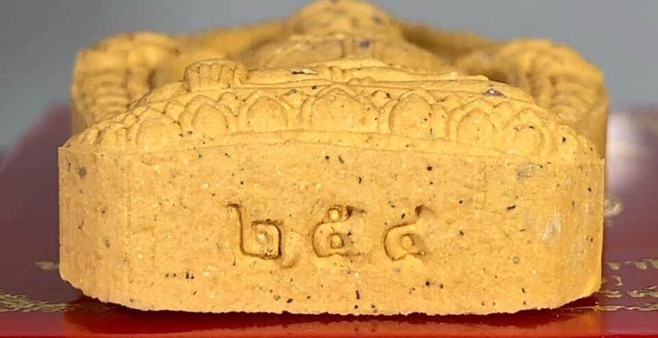 Close up yellow clay Yod Khun Phon Pak Nam Pho amulet with stamped Thai numerals and textured ornamentation