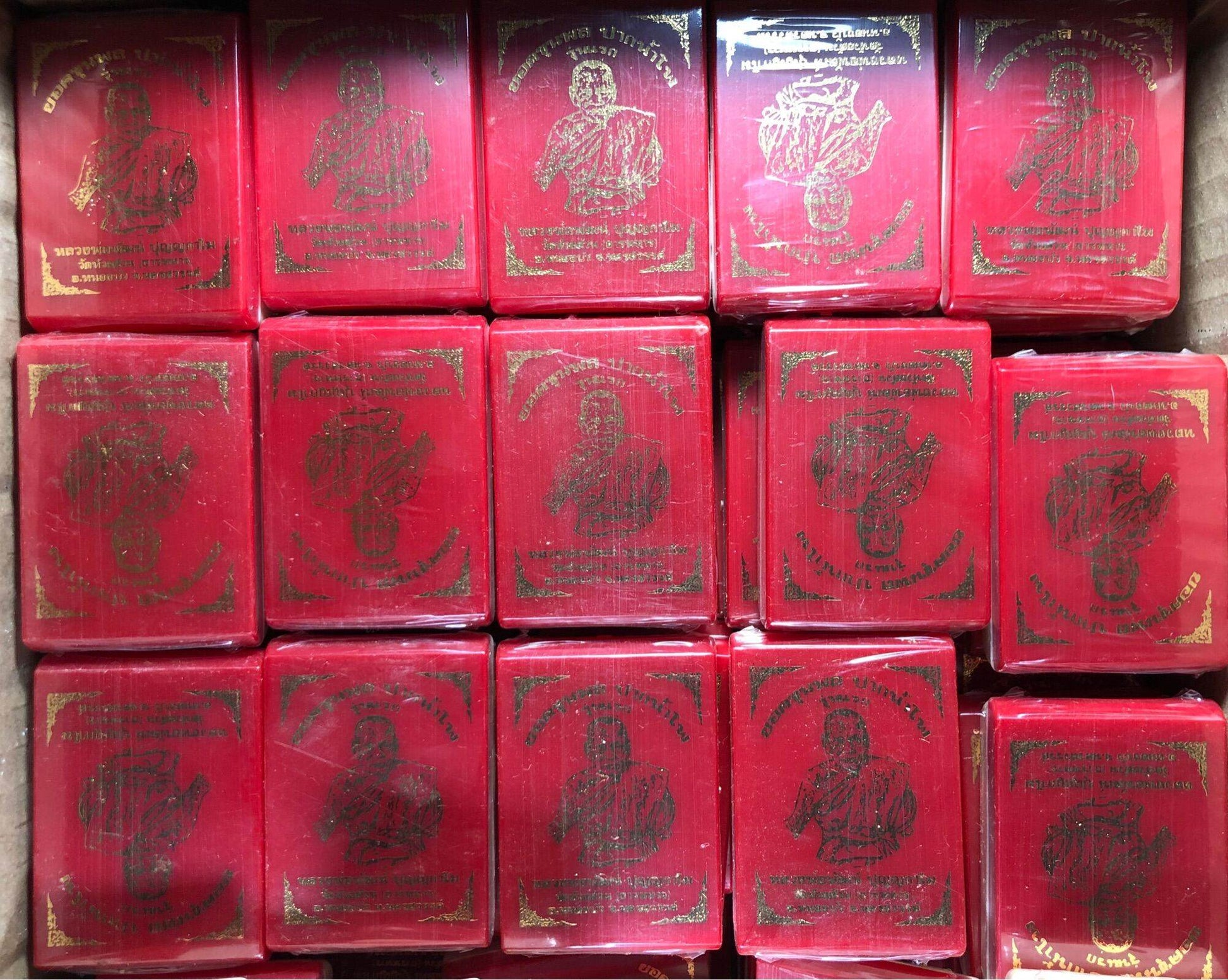 Multiple red lacquered boxes of Yod Khun Phon Pak Nam Pho amulet showing gold monk images arranged in rows