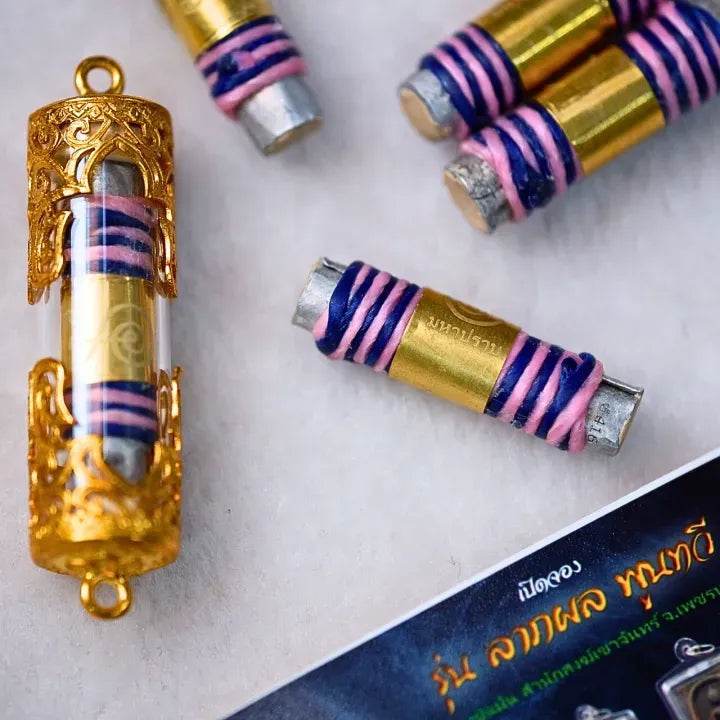 akrut Maha Prap – Protective Amulet Thai takrut cylinders wrapped in pink and blue thread with gold ornate pendant