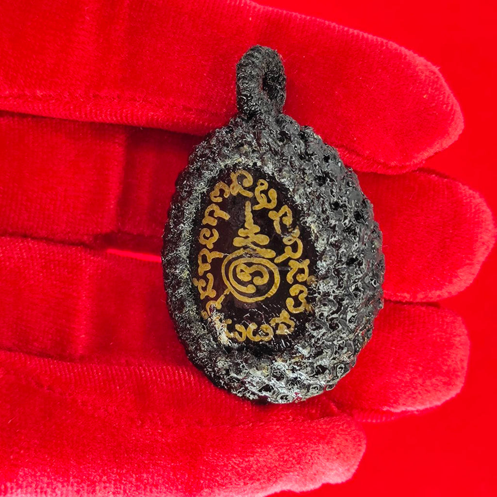 Bia Gae amulet for protection featured on a red background held in a gloved hand