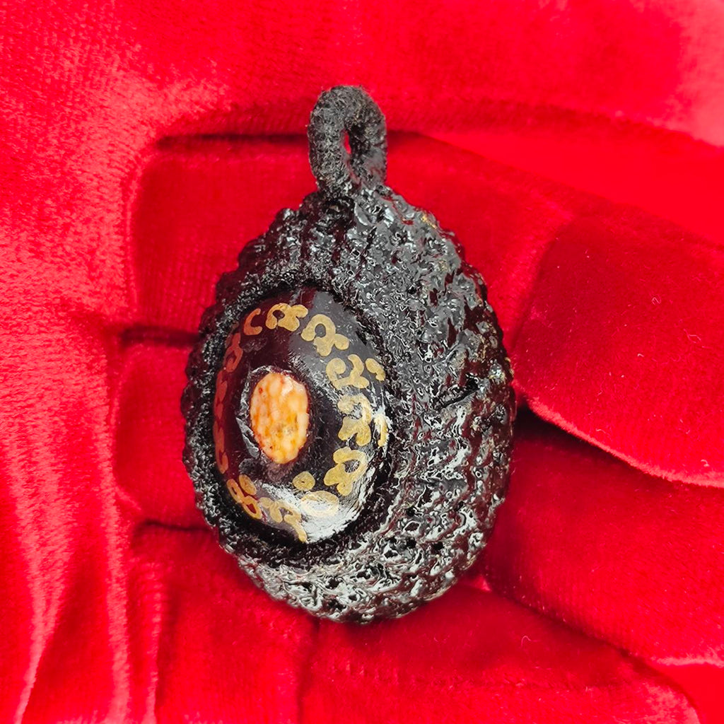 Bia Gae amulet for protection held in a red-gloved hand, featuring intricate carvings and designs.