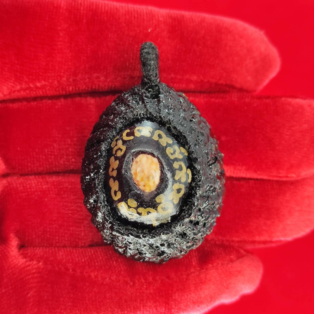 Bia Gae amulet for protection with intricate design displayed on red fabric background