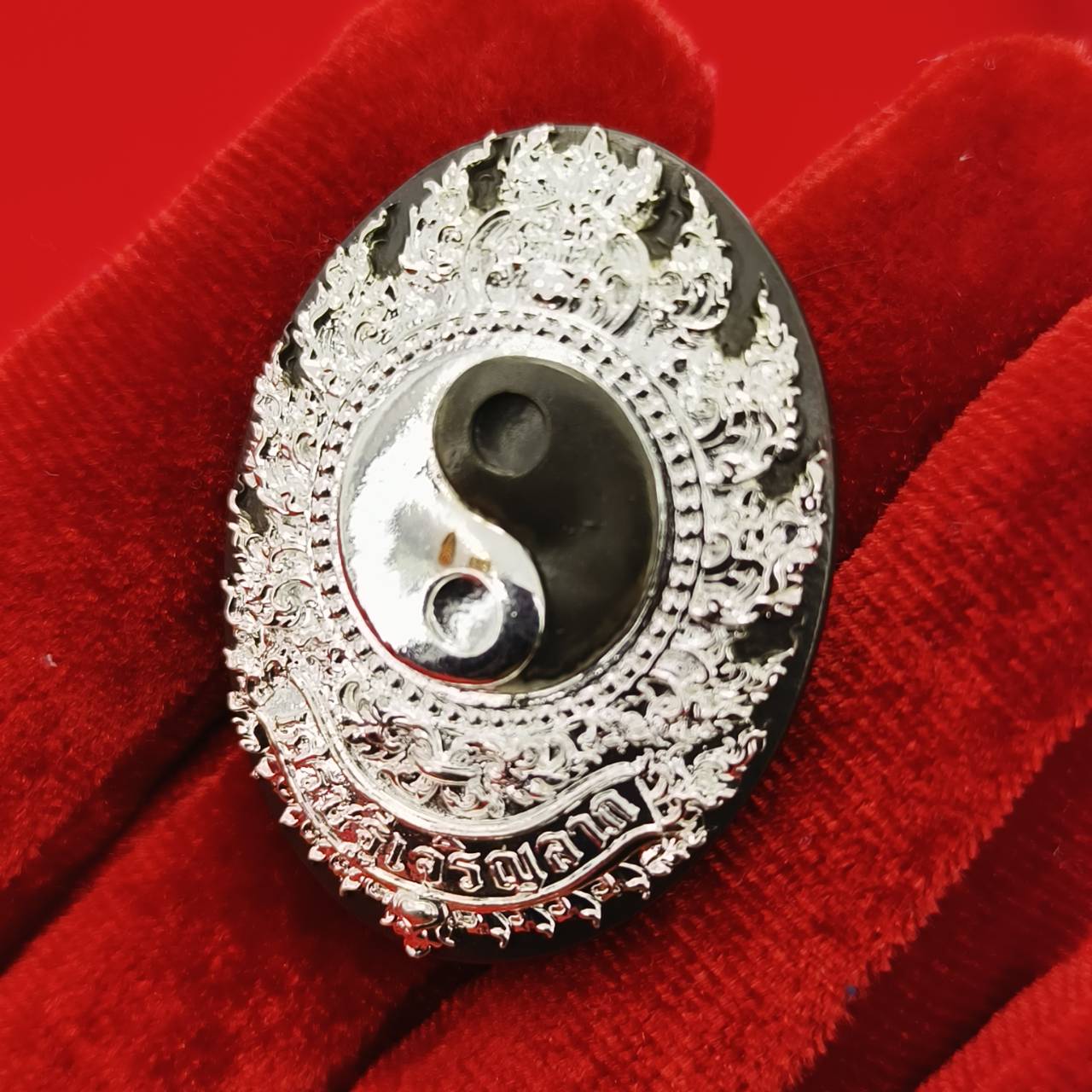 Rahu amulet coin for prosperity with intricate designs in black and silver, held on a red cloth