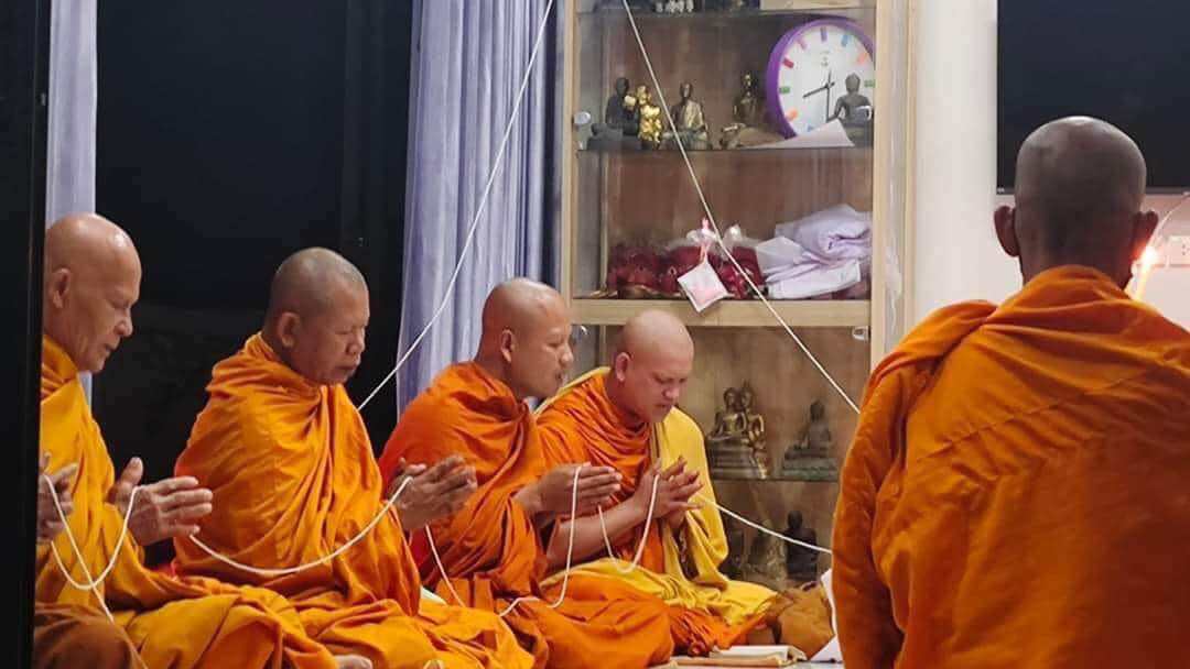 Thai monks in orange robes performing blessing ceremony with white sacred strings and statues negative energy protection charm