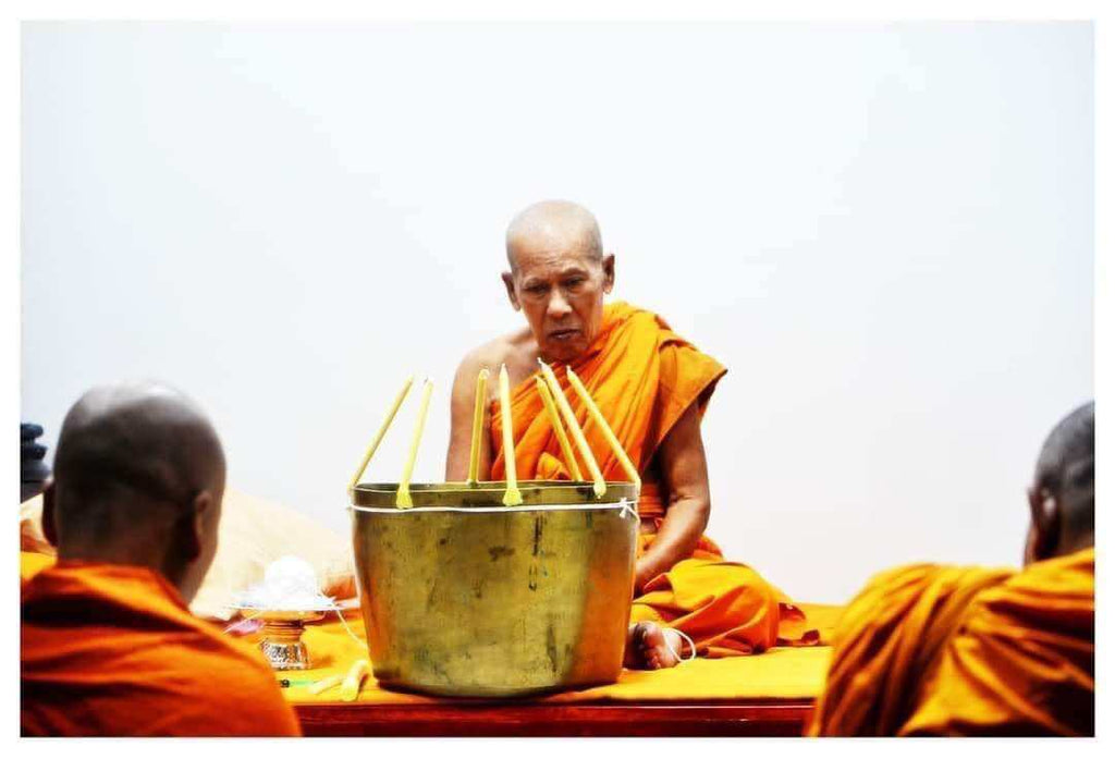 Thai monk performing blessing ritual with incense and brass bowl offering for negative energy protection charm