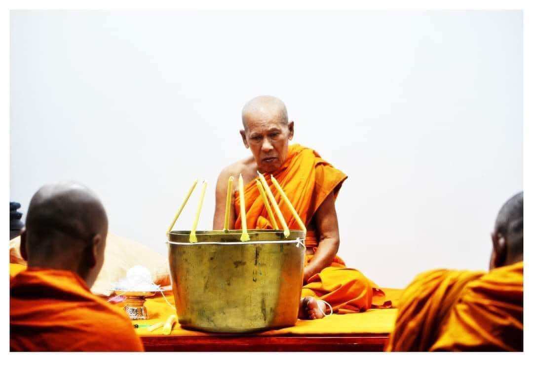 Thai monk performing blessing ritual with incense and brass bowl offering for negative energy protection charm