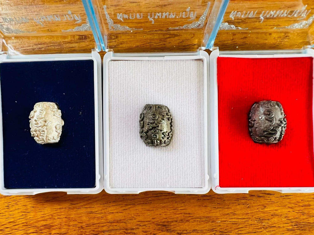 Thai Blessing Co three metal amulets in display boxes on wood background showing negative energy protection charm