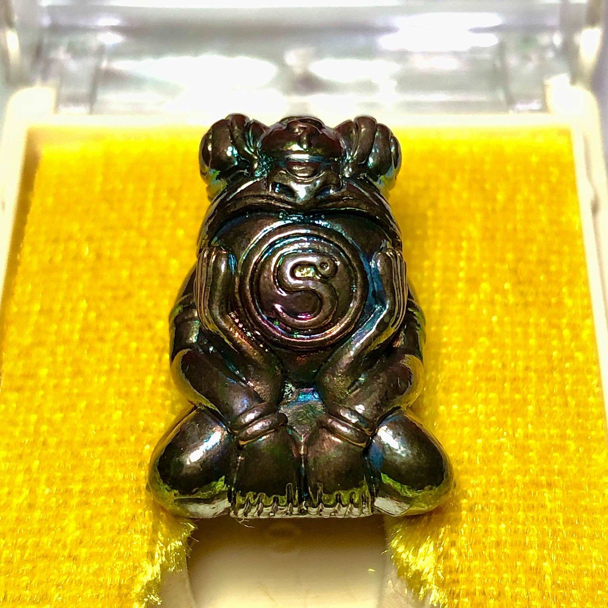 Thai Blessing Co Phaya Kob Kin Duean . metallic frog amulet pendant with spiral coin belly on yellow display