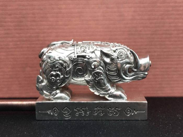 Silver Phaya Moo Setthi pig amulet statue with intricate Thai engravings on rectangular base