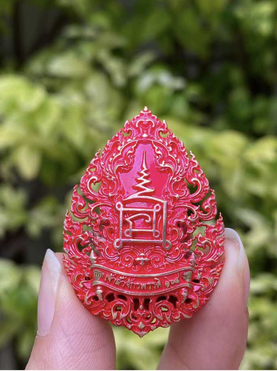 Intricately designed red Phra Pidta amulet for prosperity with decorative patterns and gold accents