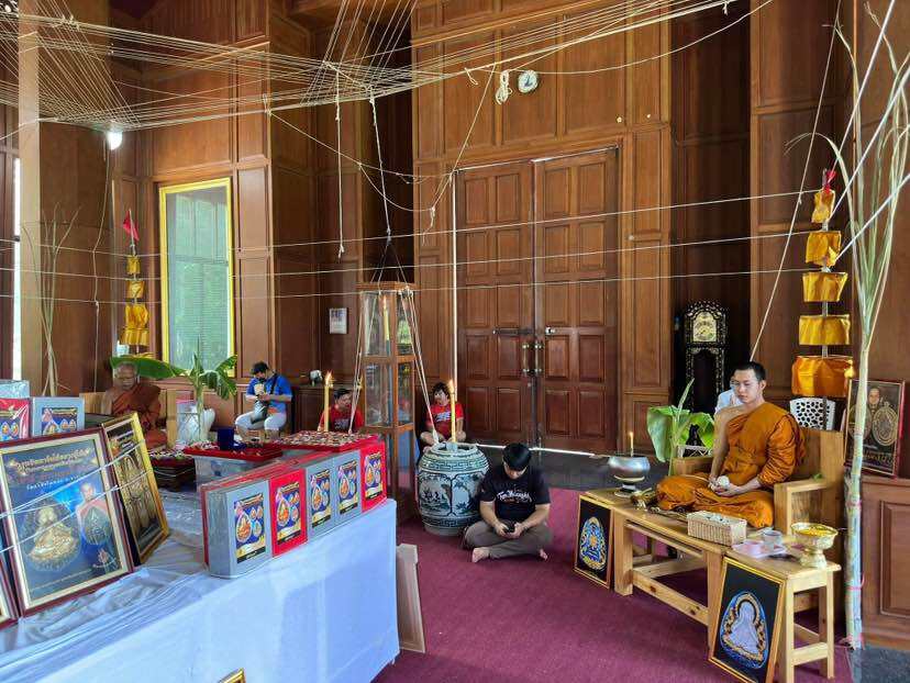 Phra Pidta amulet for prosperity displayed in a serene temple setting with monks and decorations