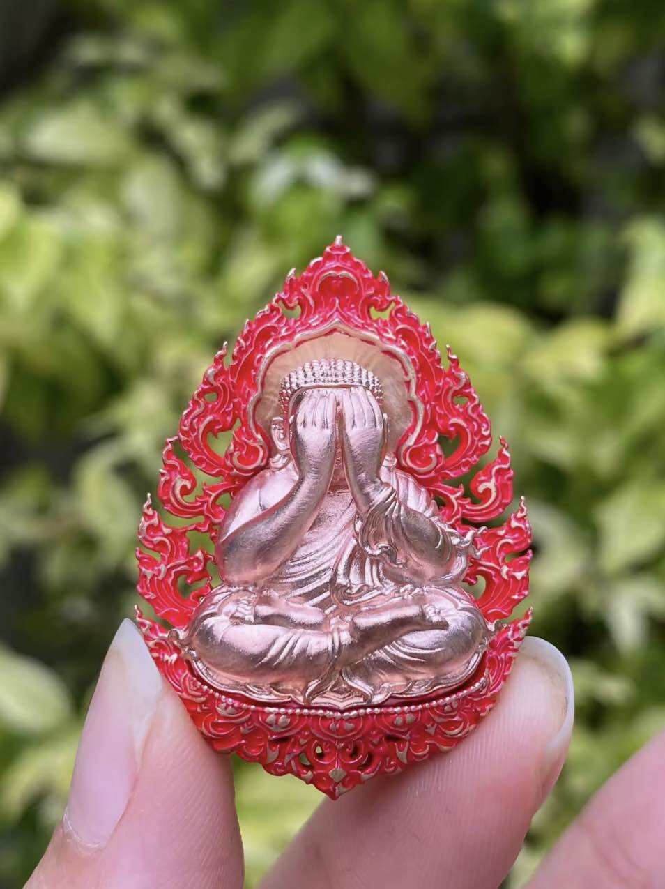Phra Pidta amulet for prosperity in red with intricate design, held by hand, symbolizing good fortune.