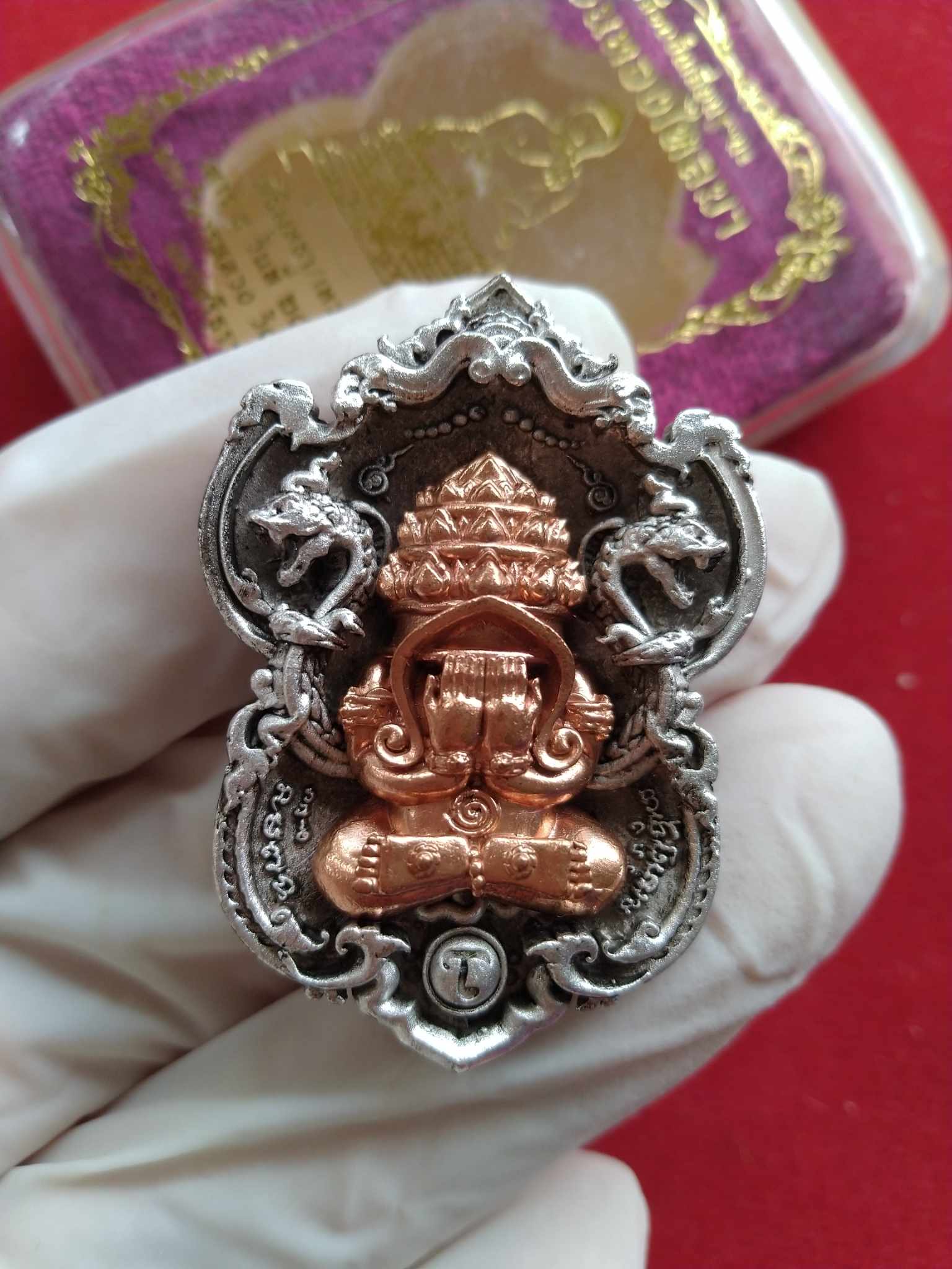 Gloved hand holding Sacred Phra Pidta Sri Maharaj Phangpakan copper and silver ornate amulet pendant