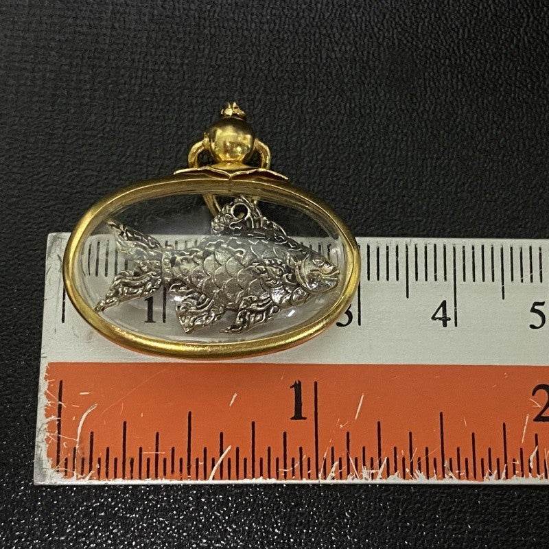 Thai Tapian fish charm for wealth silver fish pendant encased in oval gold frame next to ruler