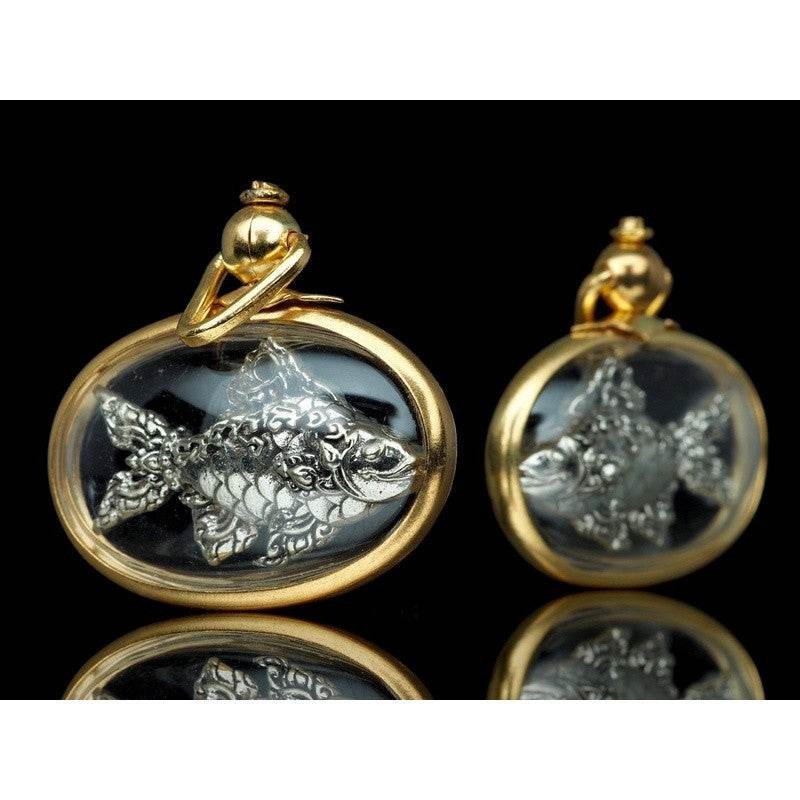 Thai Tapian fish charm for wealth silver fish amulet in gold oval pendant pair on black reflective background