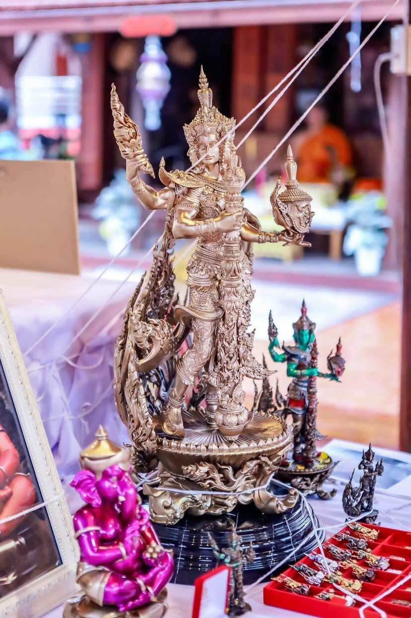 Ornate golden Thai deity statue with smaller amulets and offerings on display Thao Wessuwanno Sodaprom .