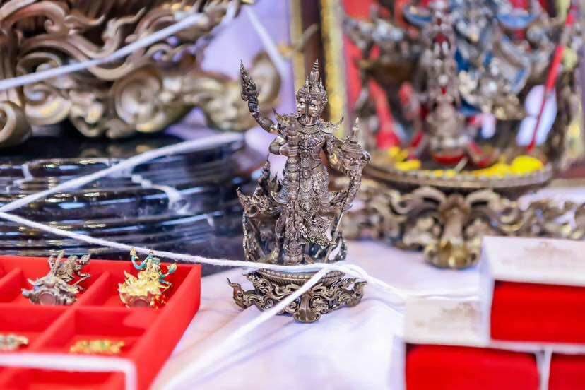Silver Thao Wessuwanno Sodaprom amulet figurine on display with small gold amulets in red boxes