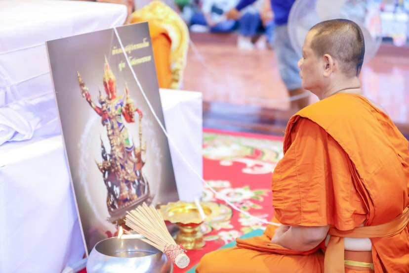 Monk in orange robes praying before Thao Wessuwanno Sodaprom amulet figurine display with incense and offerings