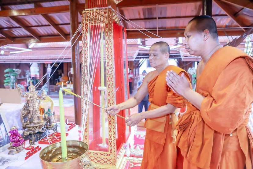 Two Buddhist monks in orange robes performing ritual at altar with amulets and figurines Thao Wessuwanno Sodaprom