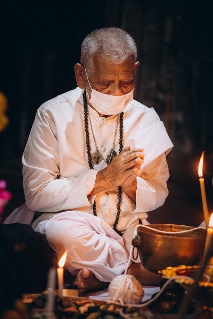 Elderly man wearing a tiger amulet for protection and praying in a spiritual setting with candles