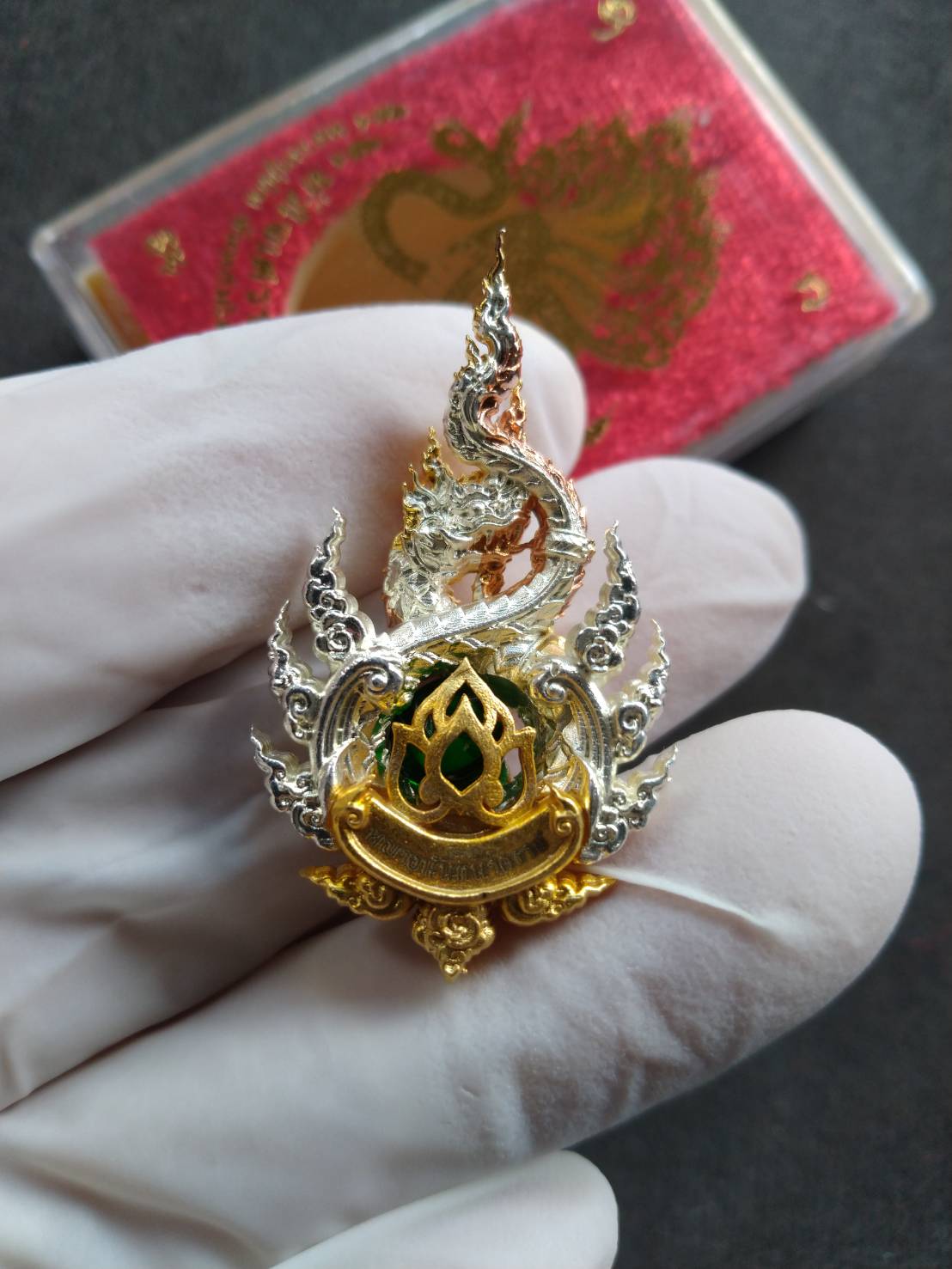 Anantanakharaj pendant Thailand ornate gold and silver Naga flame pendant with green enamel held in gloved hand