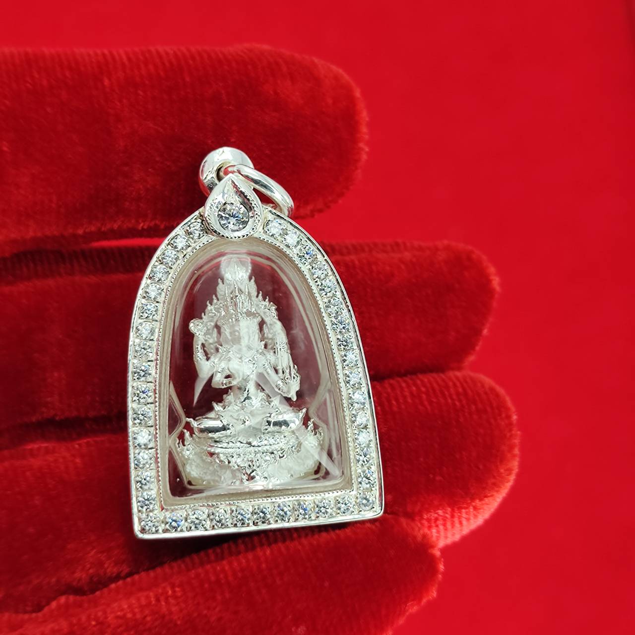 Brahma Naga amulet with silver frame pendant featuring detailed deity inside crystal case held on red velvet glove