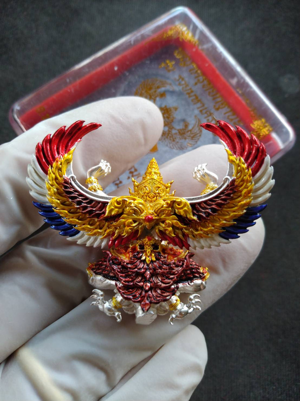 Garuda Phaya Krut Yok Tana Amulet ornate gold red blue enamel pendant held in gloved hand with case