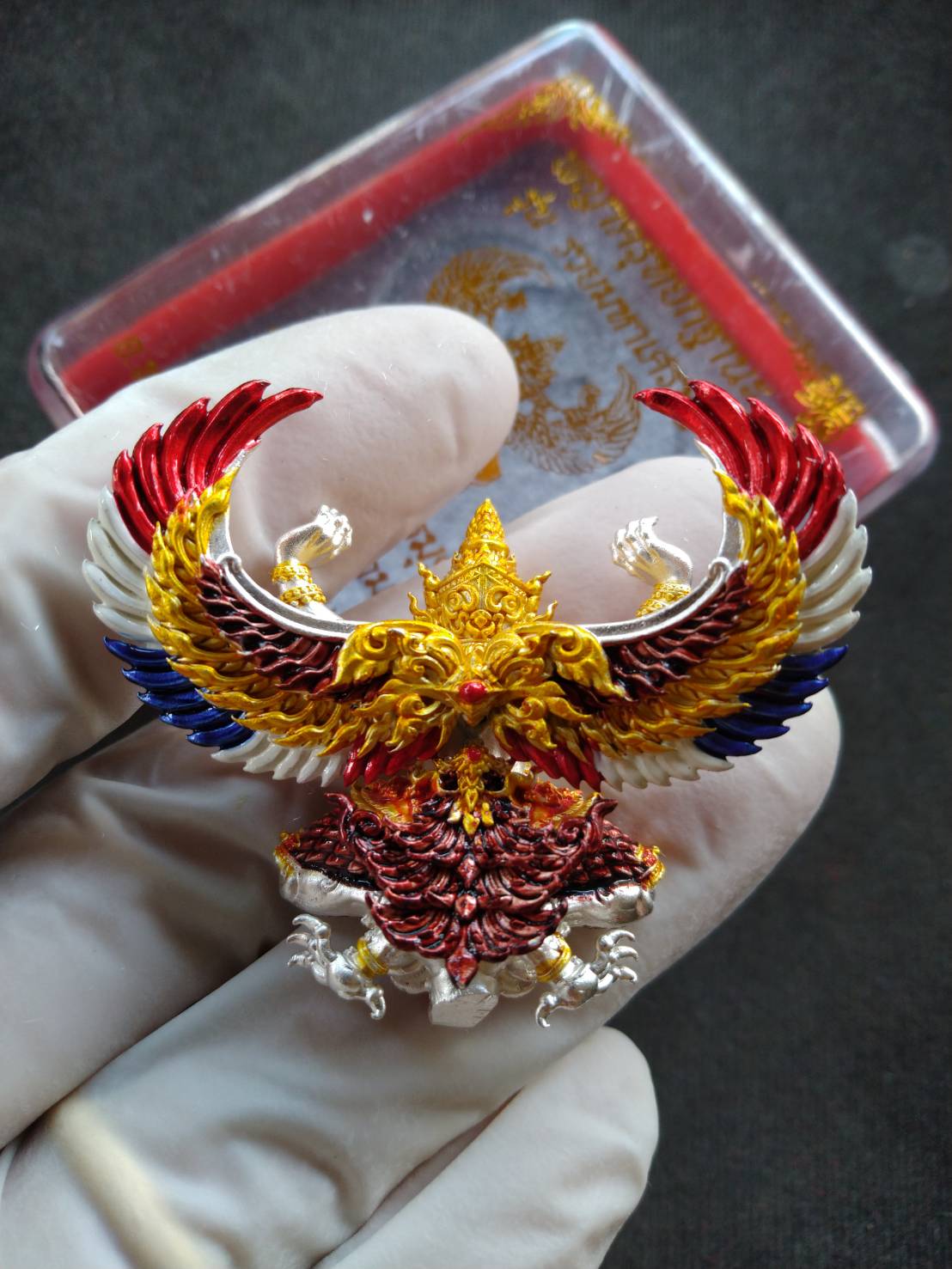 Garuda Phaya Krut Yok Tana Amulet ornate gold red blue enamel pendant held in gloved hand with case