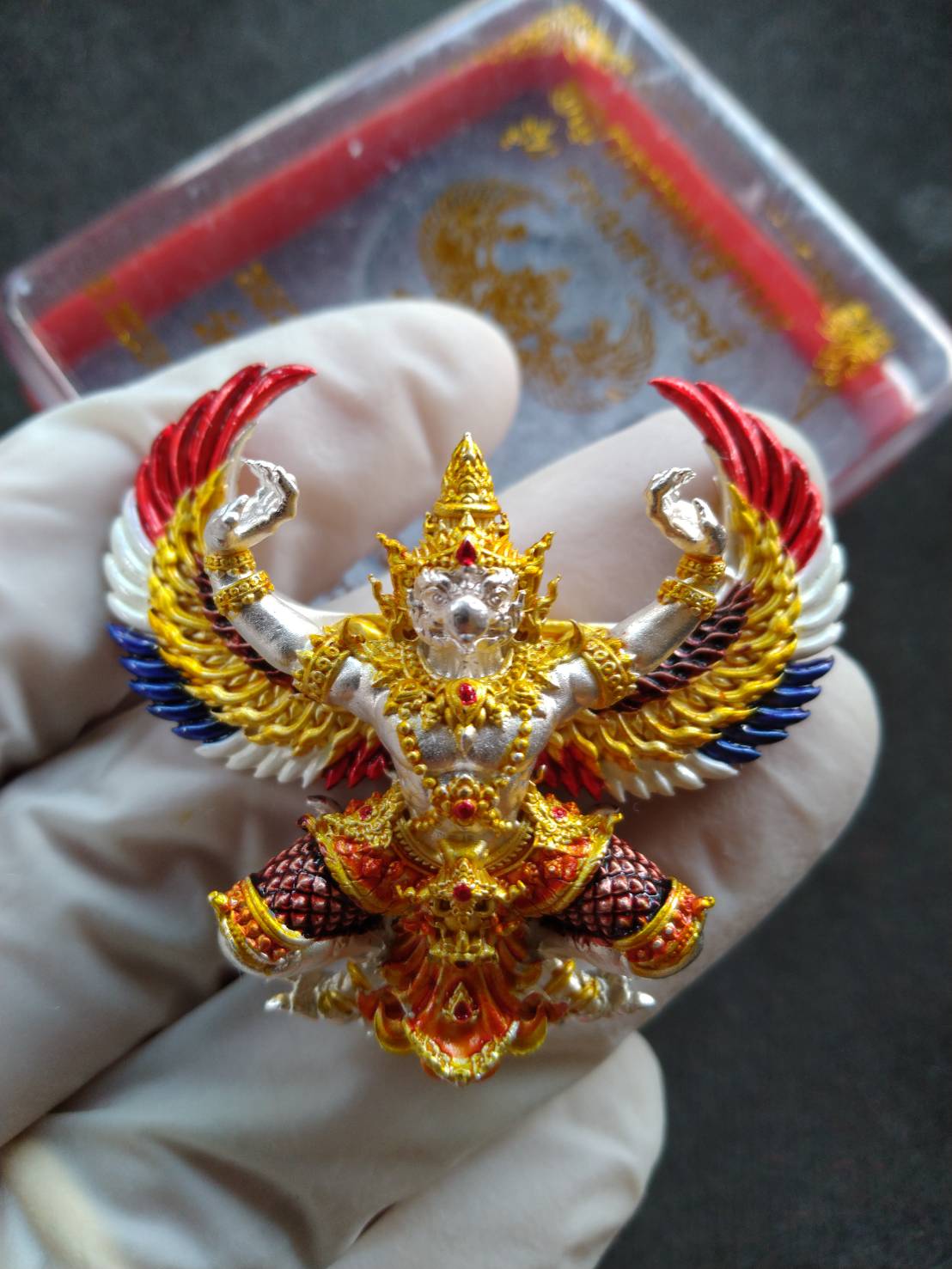 Garuda Phaya Krut Yok Tana Amulet gold red white and blue enamel pendant with intricate gilded details held in glove