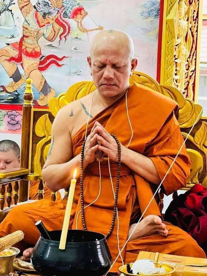 Thai monk in saffron robe holding prayer beads during blessing ceremony with ritual items Jeed Naree Phan Lak amulet