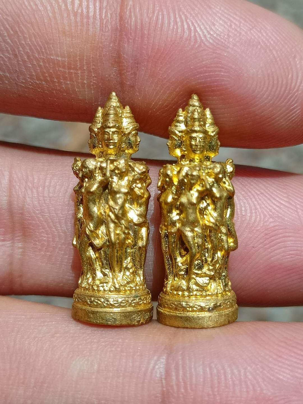 Pair of small gold Jeed Naree Phan Lak amulet pendants held between fingers showing detailed multiheaded figures