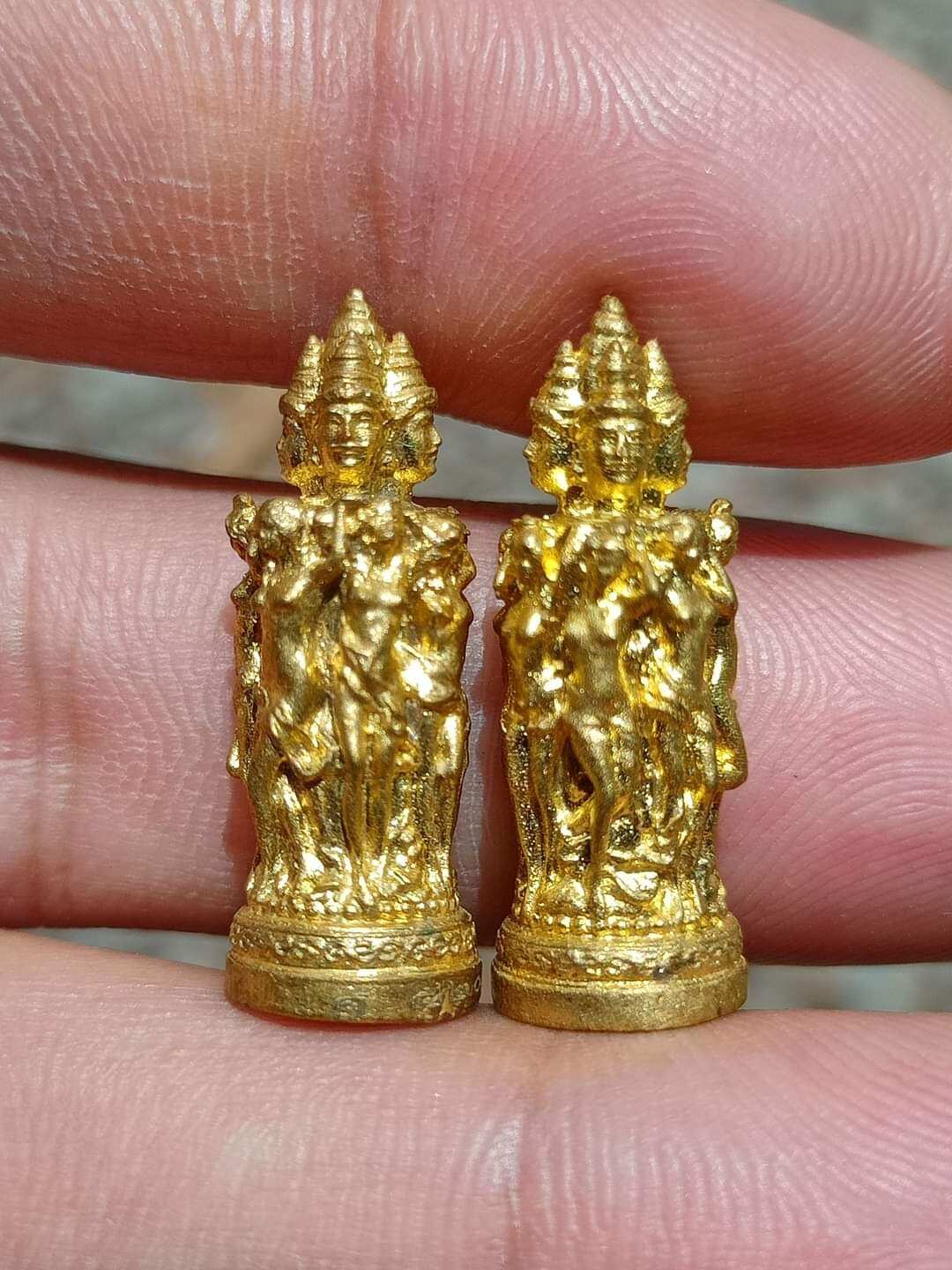 Pair of small gold Jeed Naree Phan Lak amulet pendants held between fingers showing detailed multiheaded figures