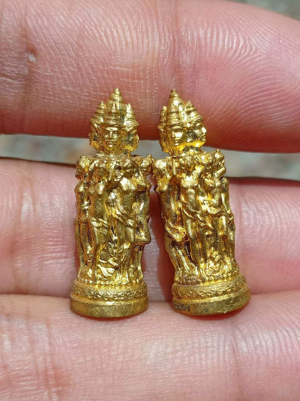 Thai Blessing Co Jeed Naree Phan Lak amulet pair in gold held on fingertips with intricate detail