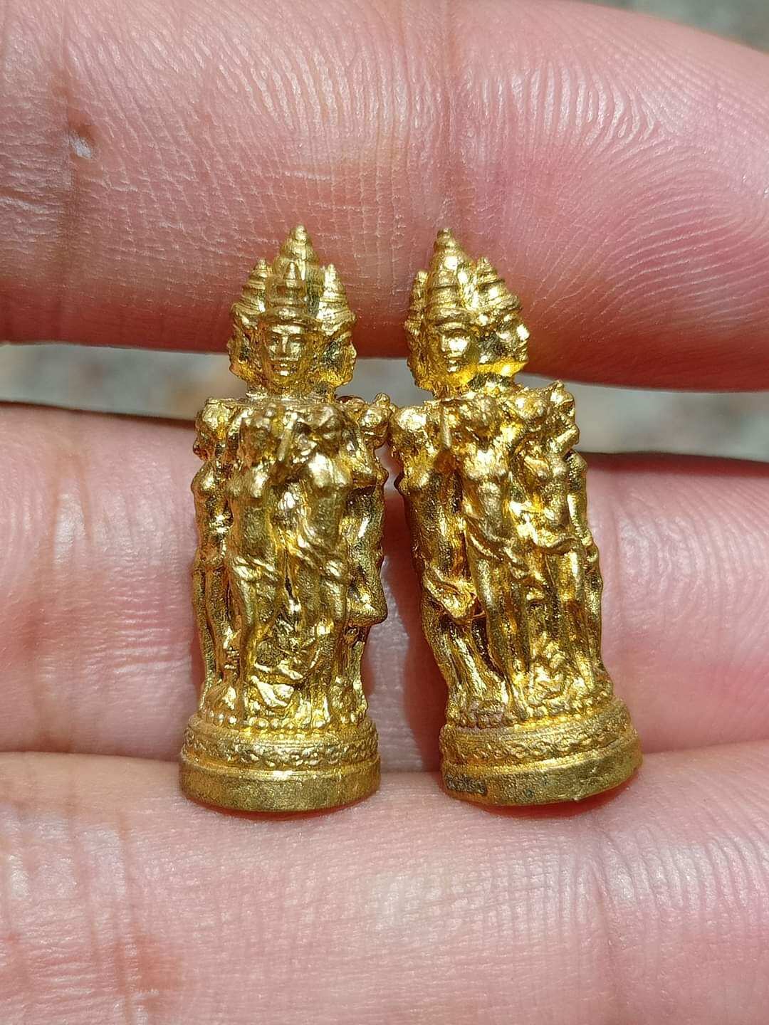 Thai Blessing Co Jeed Naree Phan Lak amulet pair in gold held on fingertips with intricate detail